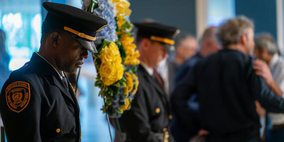 Two men in UN uniforms stand with bowed heads. A wreath is placed on a stand between them.