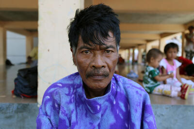 A man faces the camera with children playing in the background