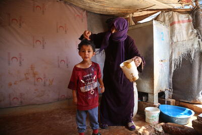 A woman pours water over a child to help him cope with the heat in Al-Hamra camp for internally displaced people in Syria’s Idleb governorate. Photo: UNA-UK/Bilal Al-Hammoud